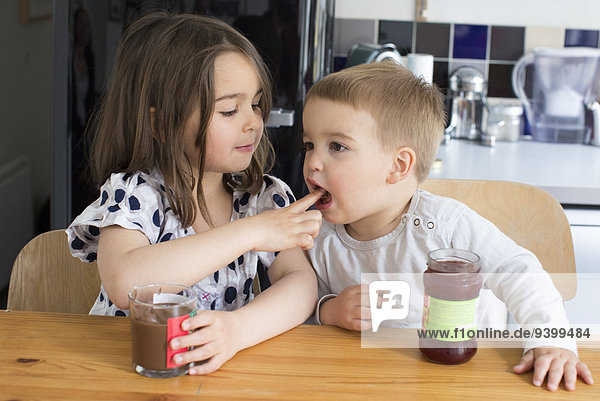 Junge Geschwister schmecken den Inhalt von Gläsern mit den Fingern.