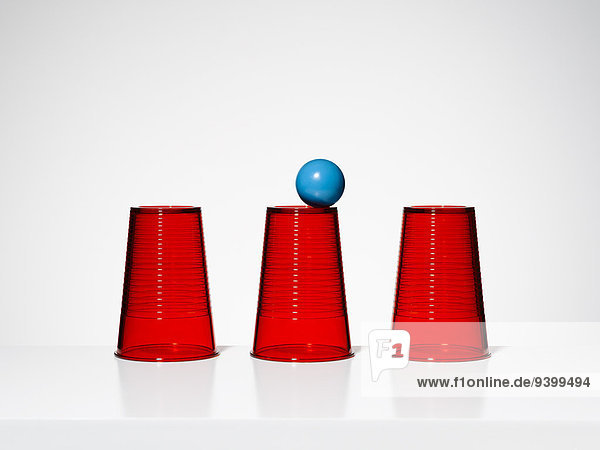 Blaue Kugel balanciert auf der Mitte von drei roten Tassen