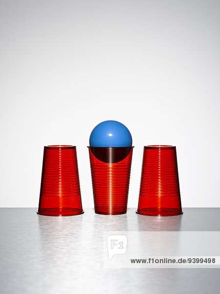 Blaue Kugel in der Mitte von drei roten Tassen