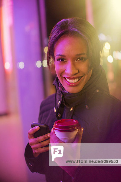 Frau auf der Stadtstraße mit Kaffee und Handy bei Nacht