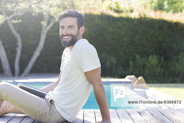 Smiling man relaxing on wooden deck by swimming pool
