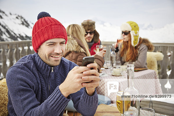 Mann mit Handy auf dem verschneiten Balkon