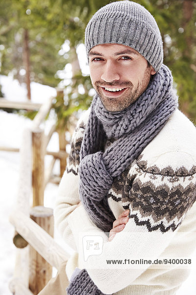 Smiling man sitting on snowy fence
