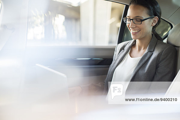 Businesswoman using laptop in car back seat