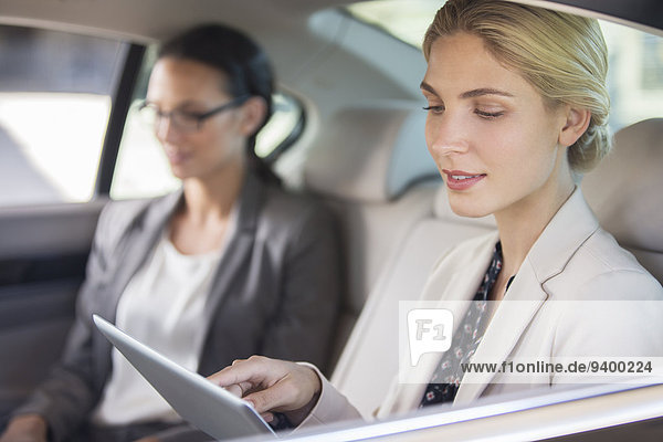 Businesswoman using digital tablet in car back seat