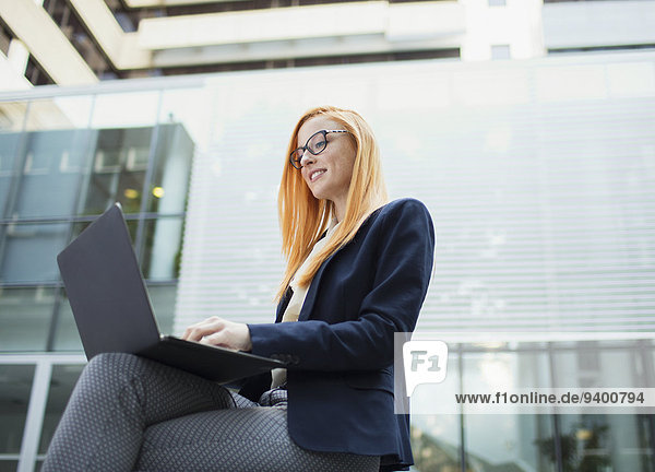 Businesswoman working on laptop outside office building