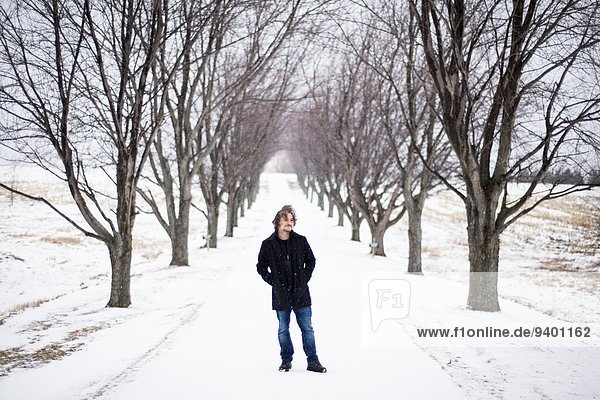 Young man stands between trees in winter