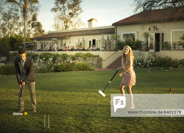 A smart young man plays croquet with a pretty young lady.
