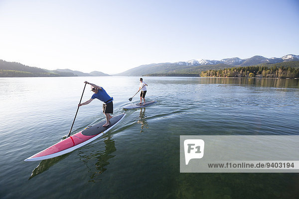 A fit male and female stand up paddle board (SUP) at sunset on Whitefish Lake in Whitefish  Montana.