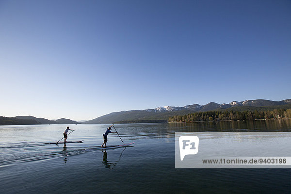 A fit male and female stand up paddle board (SUP) at sunset on Whitefish Lake in Whitefish  Montana.