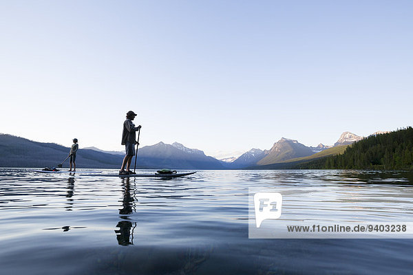 A man and woman stand up paddle boards (SUP) on Lake McDonald in Glacier National Park.