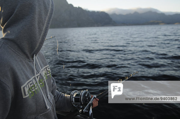 Oberkörperaufnahme Außenaufnahme Einzelperson eine Person Wasser Fischerei Sweatshirt Angel Tag halten Meer Querformat Norwegen angeln nur ein Mann Landschaft Fischer Fjord Kapuze freie Natur