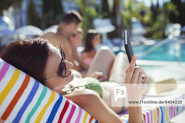 Frau beim Sonnenbaden und Texten am Schwimmbad