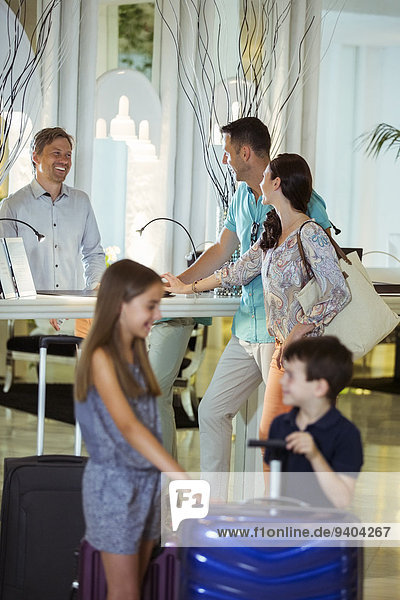Familie mit Koffern im Gespräch mit der Rezeption in der Hotellobby