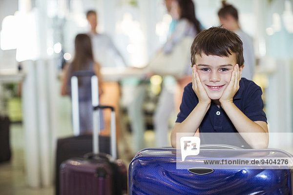 Porträt eines lächelnden Jungen,  der sich in der Hotellobby an den Koffer lehnt.