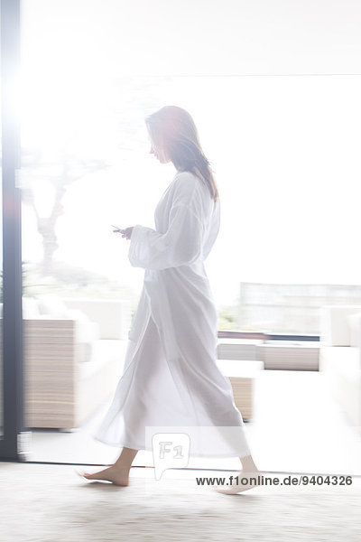 Frau im weißen Bademantel durch den modernen Flur mit Handy