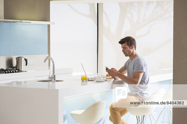Man sitting on stool at kitchen island and using phone