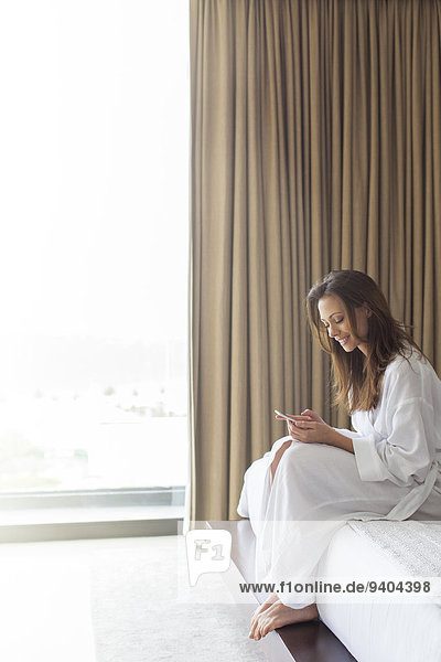 Lächelnde Frau im Bademantel SMS im Schlafzimmer