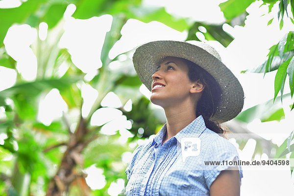 Lächelnde Frau mit Strohhut und Blick auf Pflanzen im sonnigen Garten