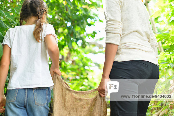 Rear view of woman and girl carrying burlap sack through garden
