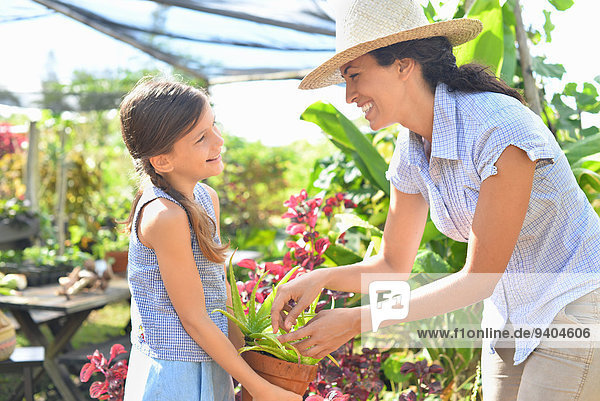 Lächelnde Frau und Mädchen mit Topfpflanze im sonnigen Gewächshaus