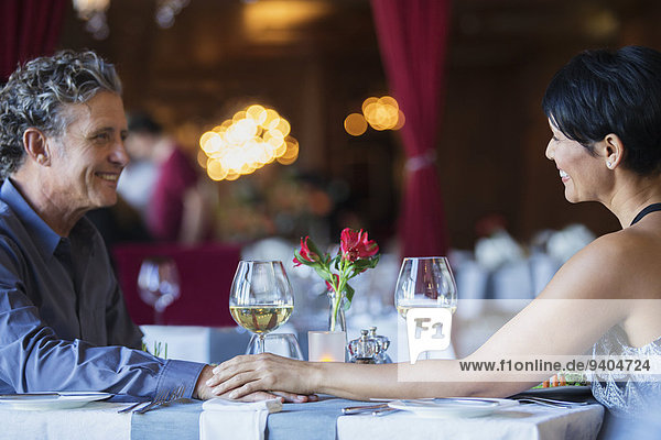 Ein reifes Paar sitzt von Angesicht zu Angesicht und hält die Hände am Restauranttisch.