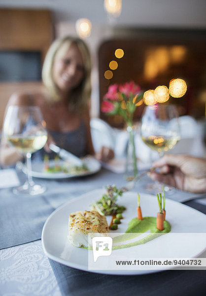 Nahaufnahme von Teller mit Fisch und Karotten auf Restauranttisch  Frau im Hintergrund