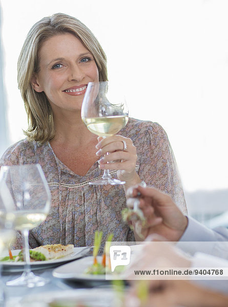Porträt einer lächelnden Frau mit einem Glas Weißwein am Restauranttisch