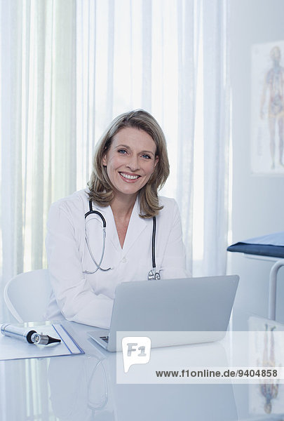 Portrait einer lächelnden Ärztin am Schreibtisch mit Laptop