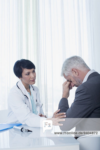 Ärztin am Schreibtisch sitzend und tröstend traurige Patientin