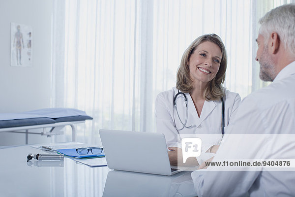 Lächelnde Ärztin im Gespräch mit Patientin am Schreibtisch im Büro