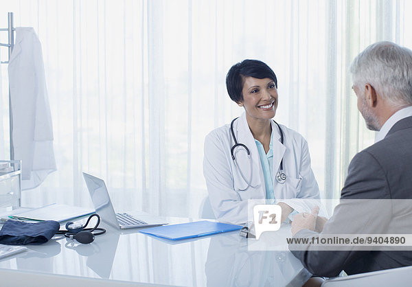 Smiling female doctor talking to patient at desk in office