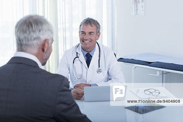 Smiling mature doctor and man sitting at desk in office