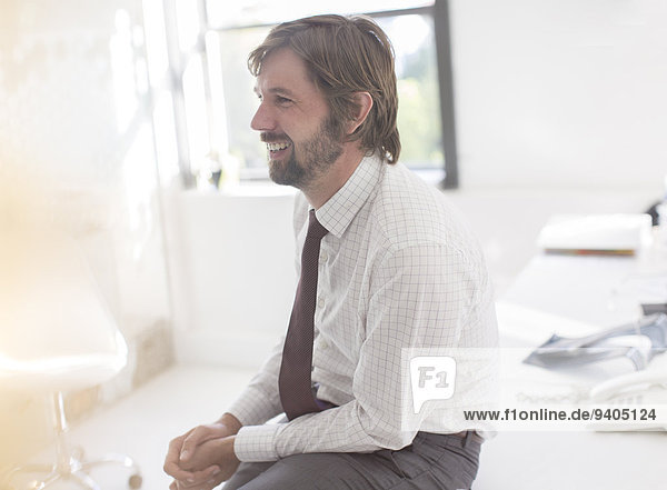 Smiling businessman wearing shirt and tie sitting on desk in office