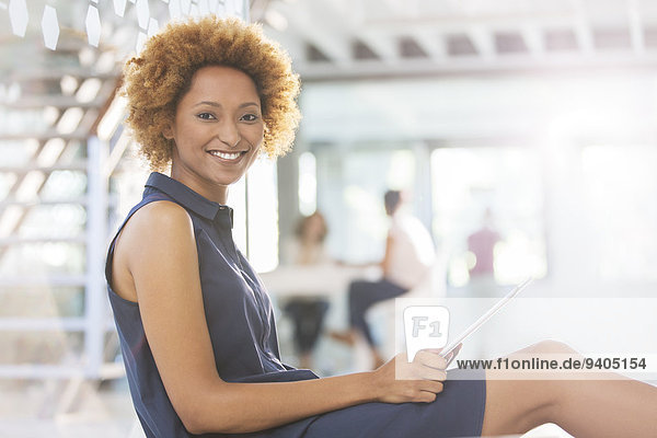 Porträt einer lächelnden Frau mit digitalem Tablett im Büroflur  Kollegen im Hintergrund