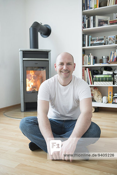 Portrait of man sitting in his living room with fireplace  smiling