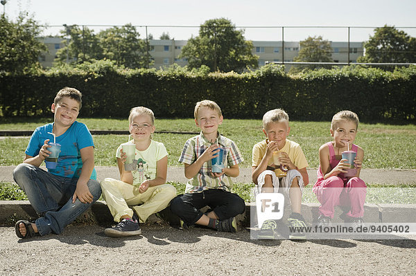 Children with mugs sitting together at curb