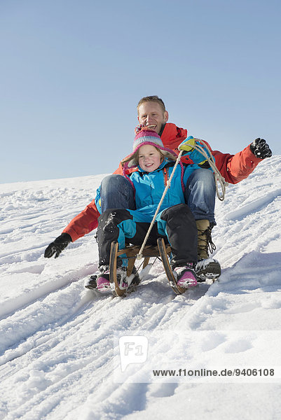 Father and daughter sledging down hill  smiling