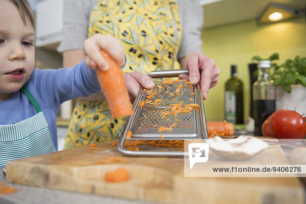 Boy helping his mother to grate carrots in kitchen