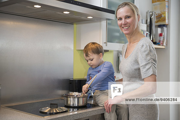 Boy helping his mother stirring food in pot  smiling