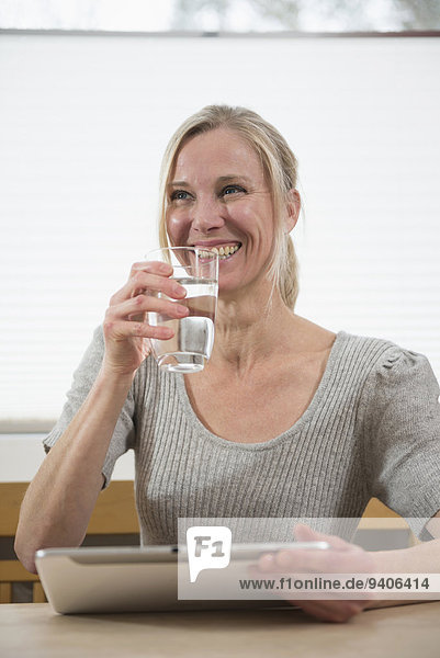 Woman with glass of water and digital tablet  smiling