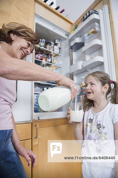 Grandmother pouring milk into glass for granddaughter