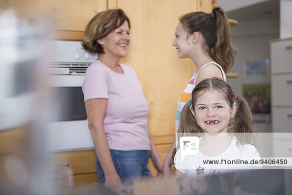 Portrait of girl  grandmother and sister looking into refrigerator in background