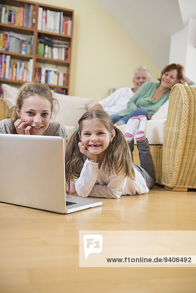 Granddaughters using laptop while grandparents in background