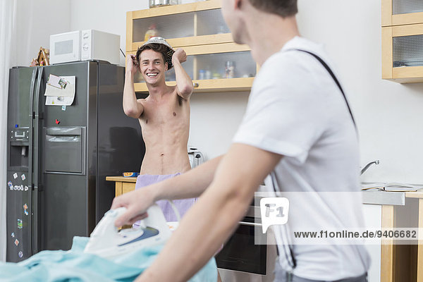 Man making mischief while another man ironing clothes