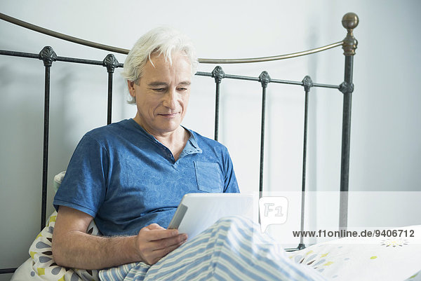 sitzend benutzen Mann lächeln Bett reifer Erwachsene reife Erwachsene Tablet PC