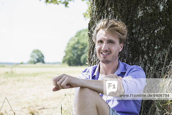 Portrait of mid adult man sitting under tree  smiling