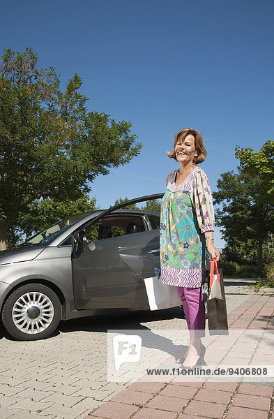 Senior woman holding shopping bags near car
