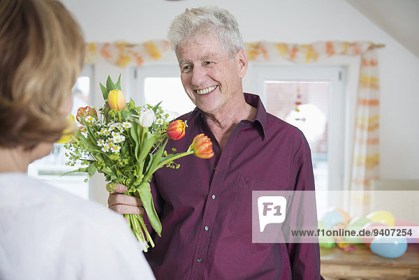 Senior man hand over bouquet to woman on birthday  smiling
