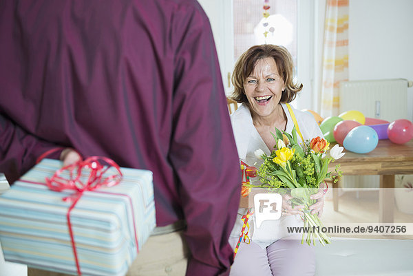 Senior man hand over present to woman on birthday  smiling